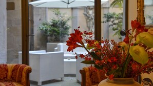 A room with a large window, a vase of red flowers, and a white umbrella outside. - Hotel San Michele (Cortona)
