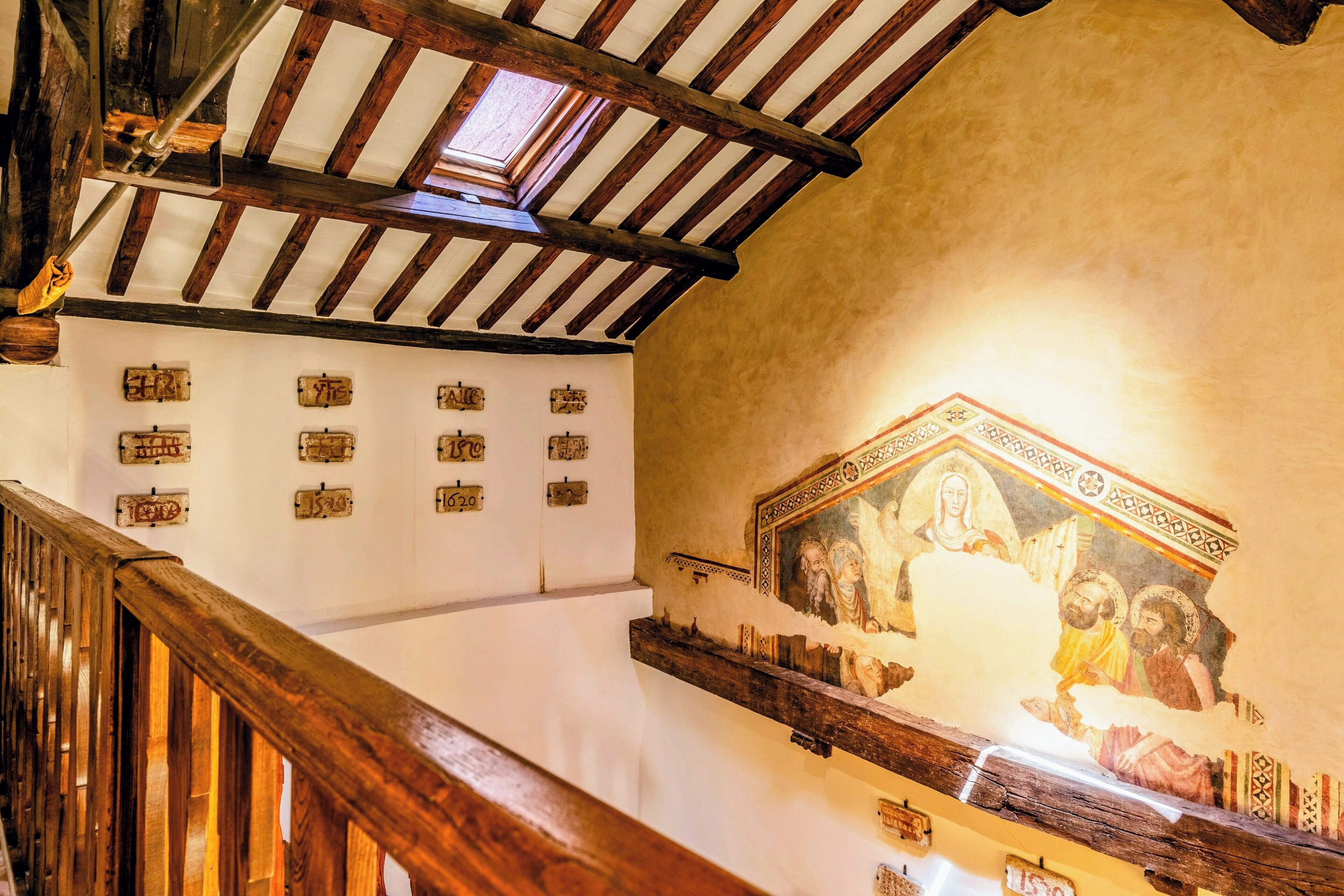 Un escalier avec des rampes en bois et un plafond voûté aux poutres apparentes.