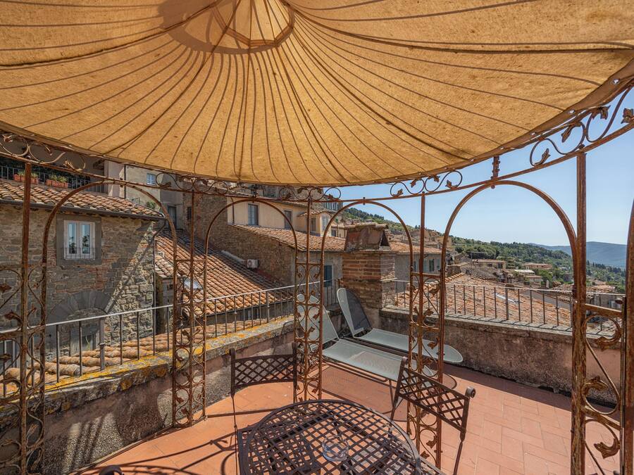 Una terraza en la azotea con una mesa y sillas de metal, un parasol grande y vistas de la ciudad.