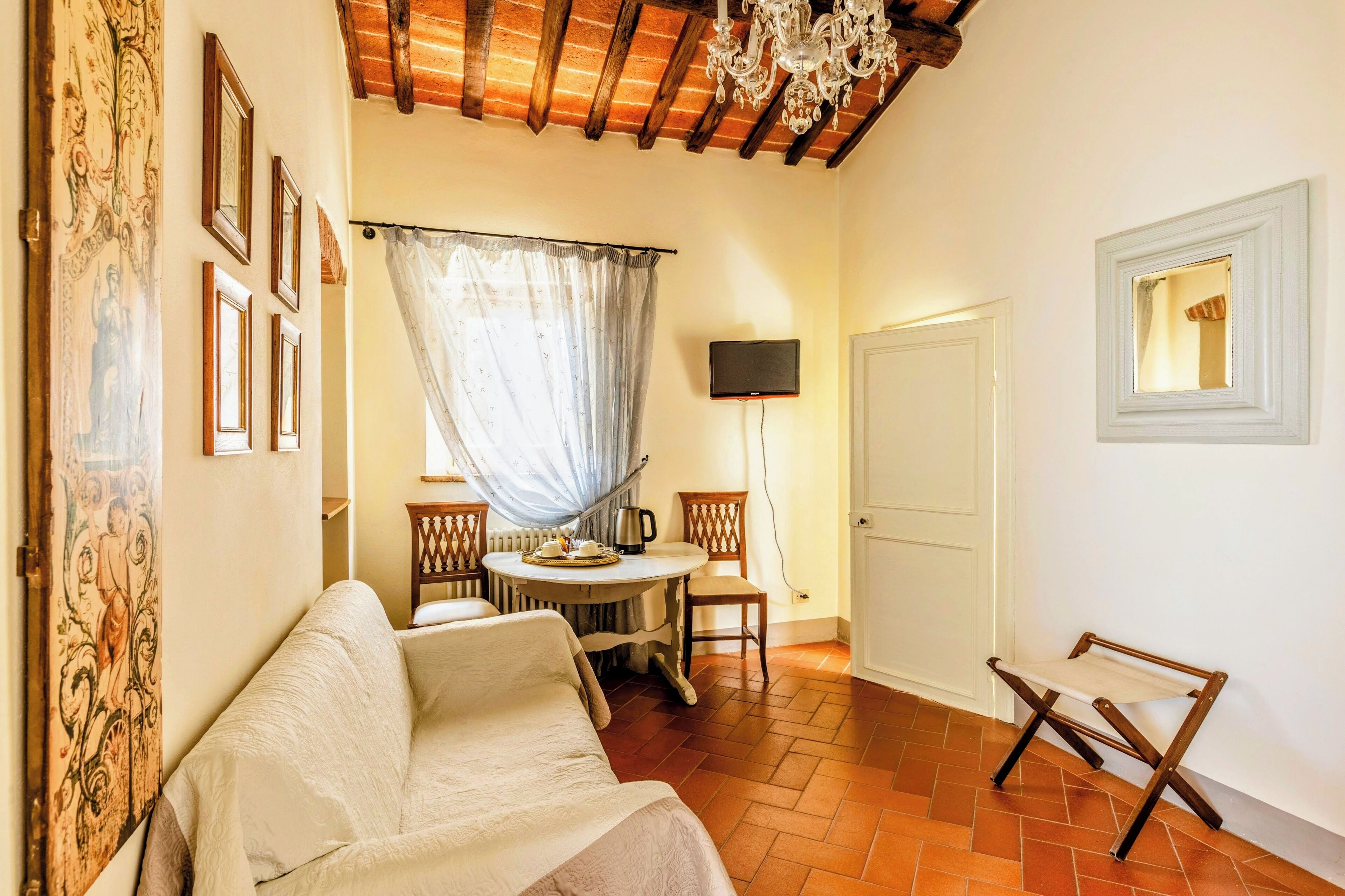 A cozy room with a sofa, a small round table with a kettle, chairs, a TV, and a door.