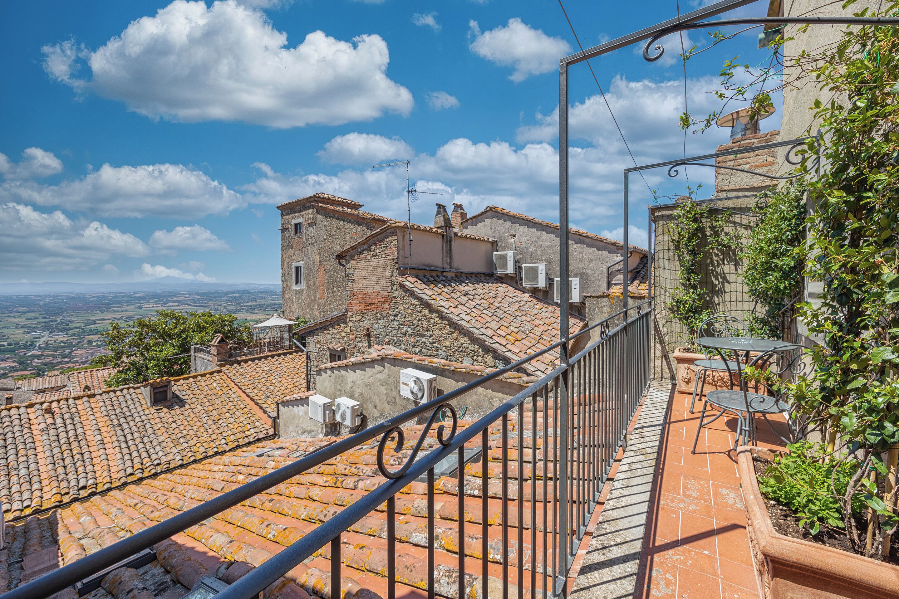 Una terraza con suelo de baldosas, barandilla metálica y vistas a la ciudad.