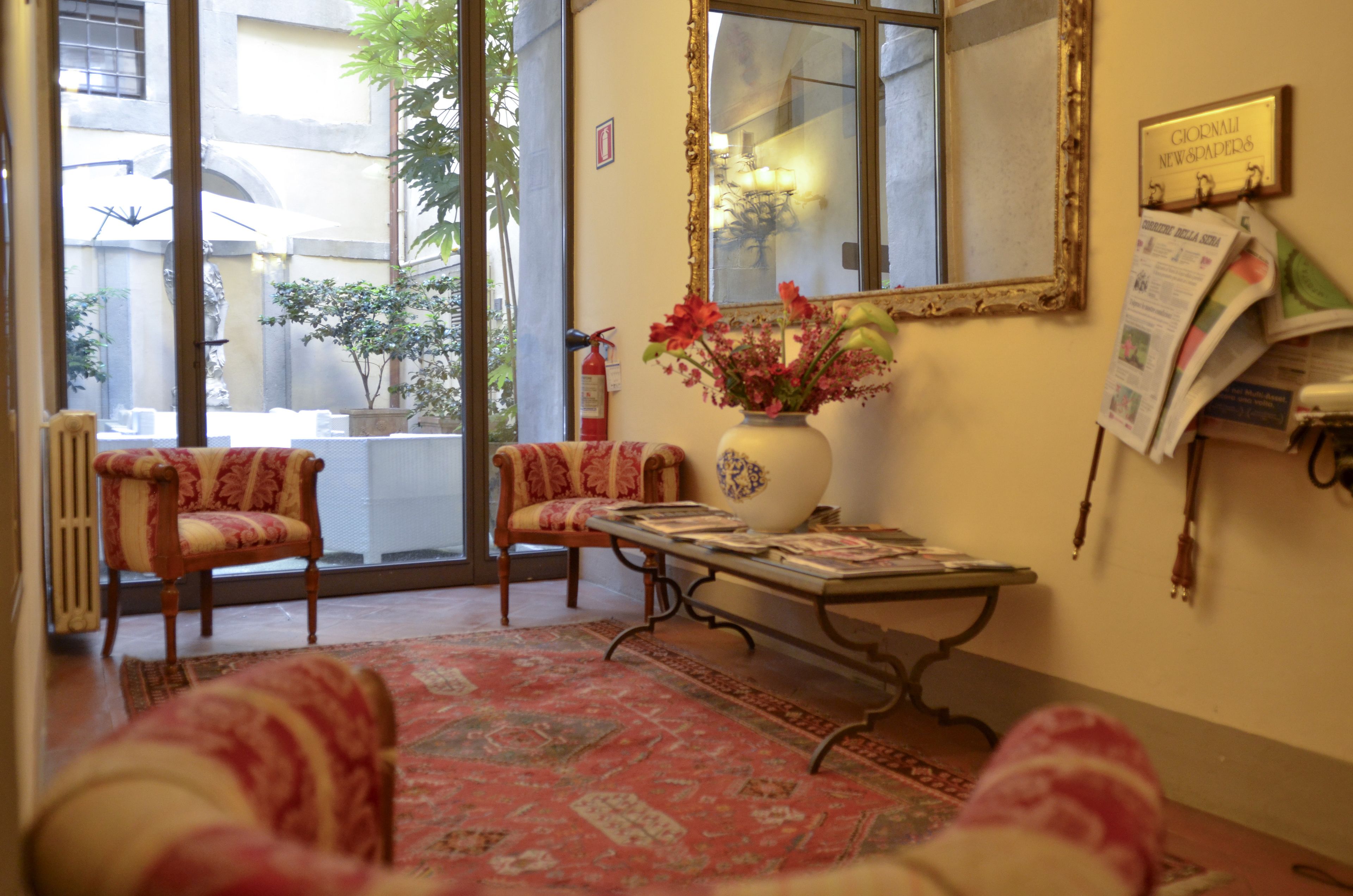 A room with two armchairs, a table with newspapers, a vase with flowers, and a mirror on the wall.