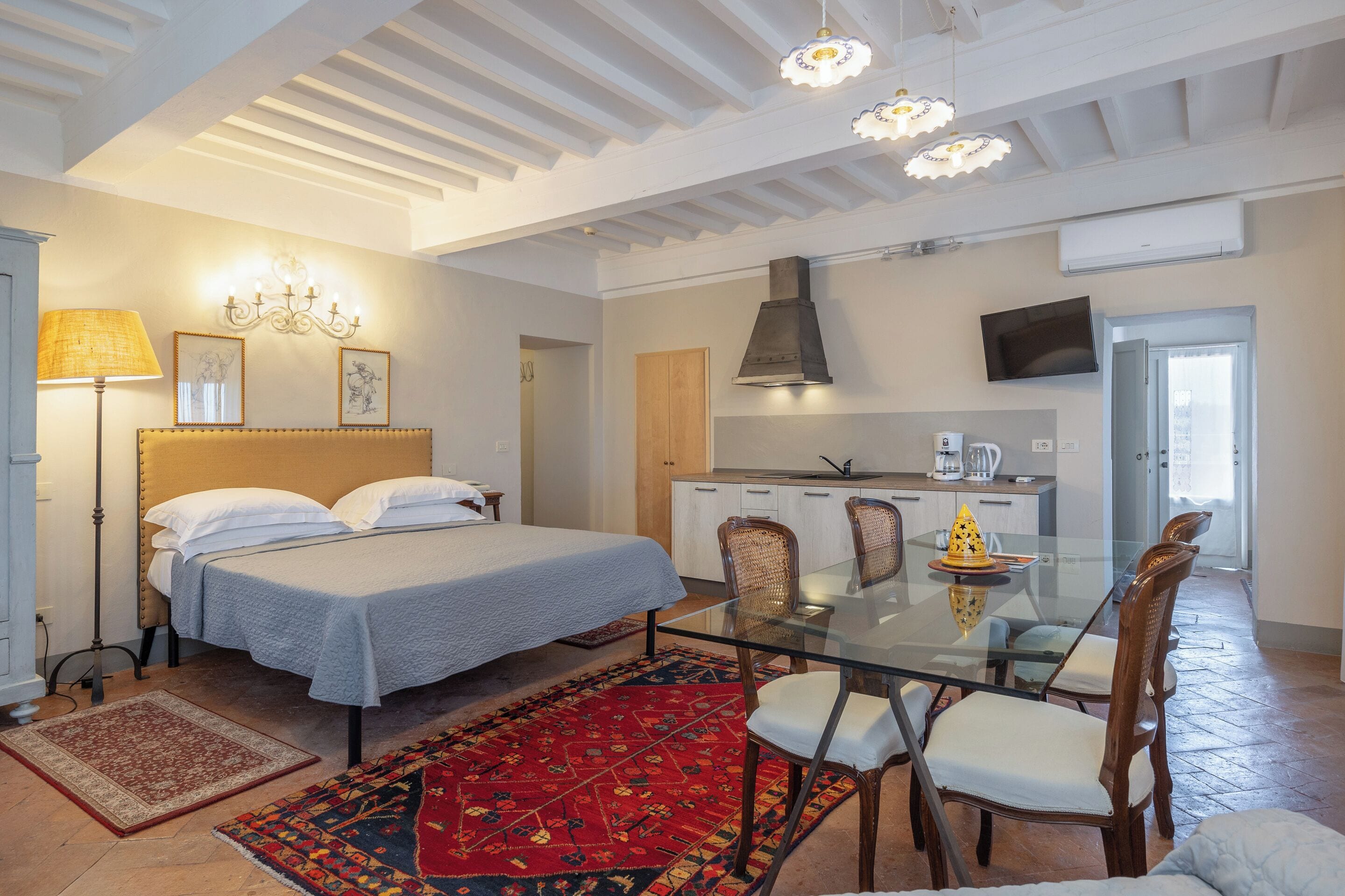 A bedroom with a bed, bedside lamp, and a dining area with chairs and a table.