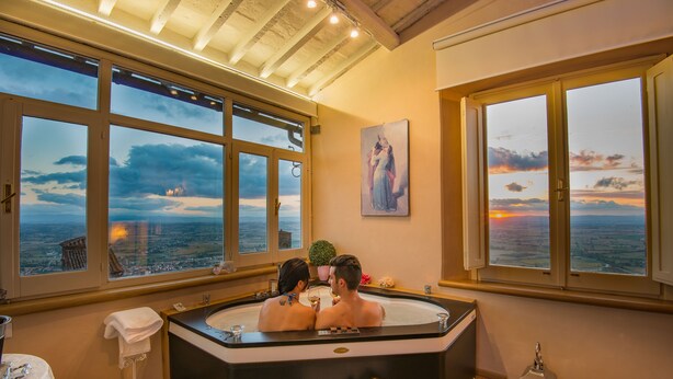 A couple in a hot tub with a cityscape view through large windows. - Hotel San Michele (Cortona)