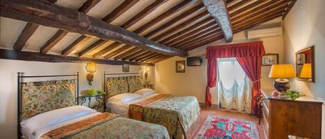A bedroom with two beds, wooden beams on the ceiling, a red curtain, and a small table with a lamp.