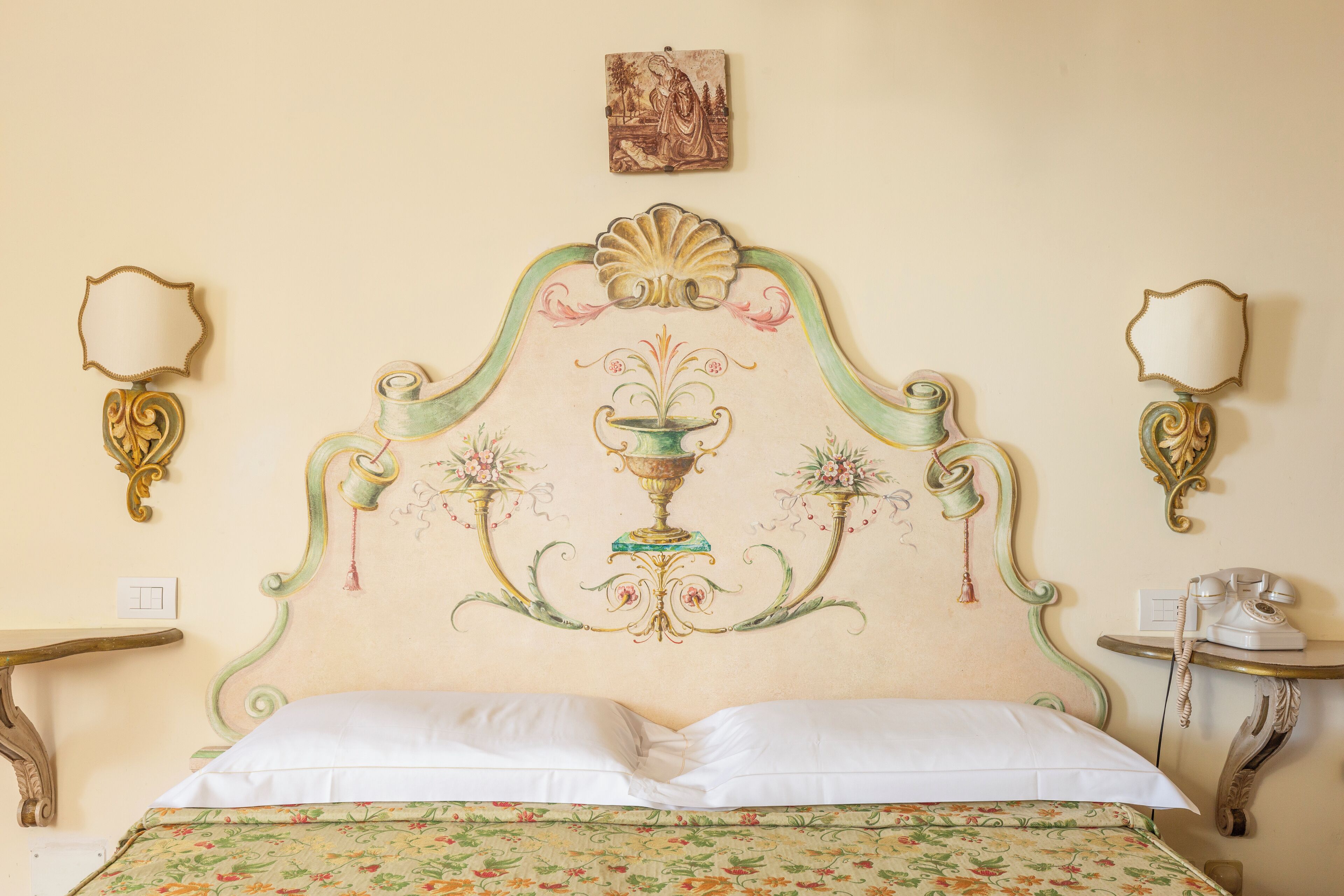 Una cama con una colcha estampada, un cabecero decorativo con un jarrón central y dos espejos colgados en la pared.
