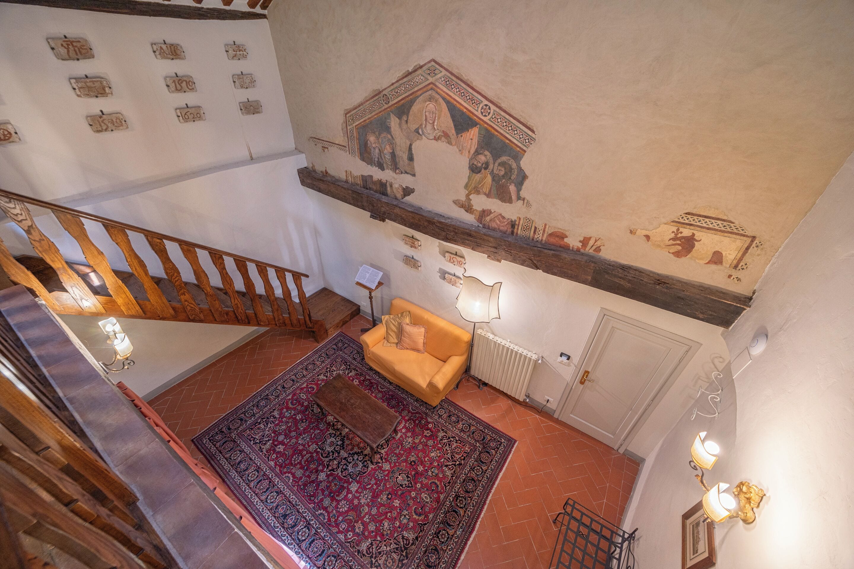 Une pièce avec un escalier, un tapis à motifs, un canapé et un mur orné d’une fresque.