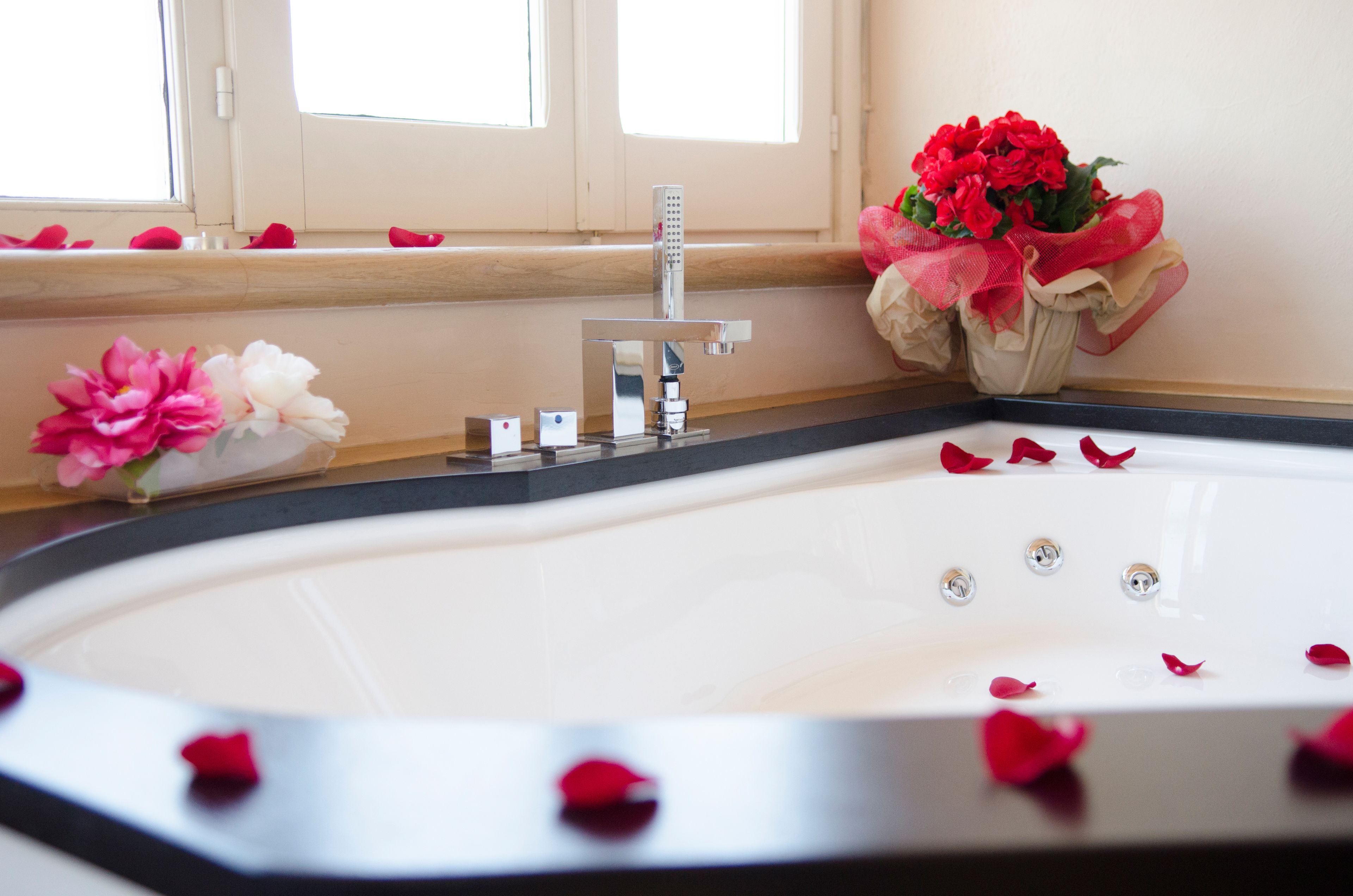 A bathroom with a bathtub, a window with rose petals, and a bouquet of flowers.