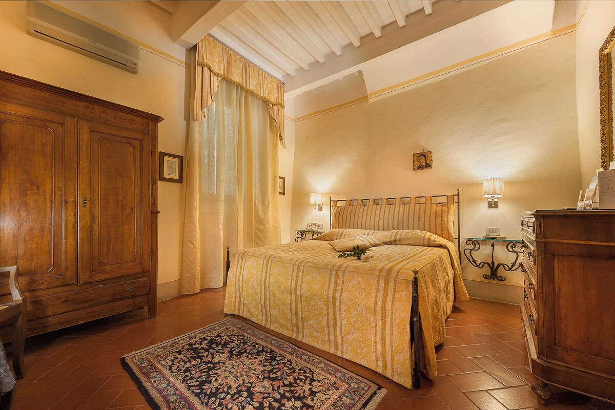 A bedroom with a large wooden wardrobe, a bed with a patterned bedspread, a decorative rug, and a chandelier.