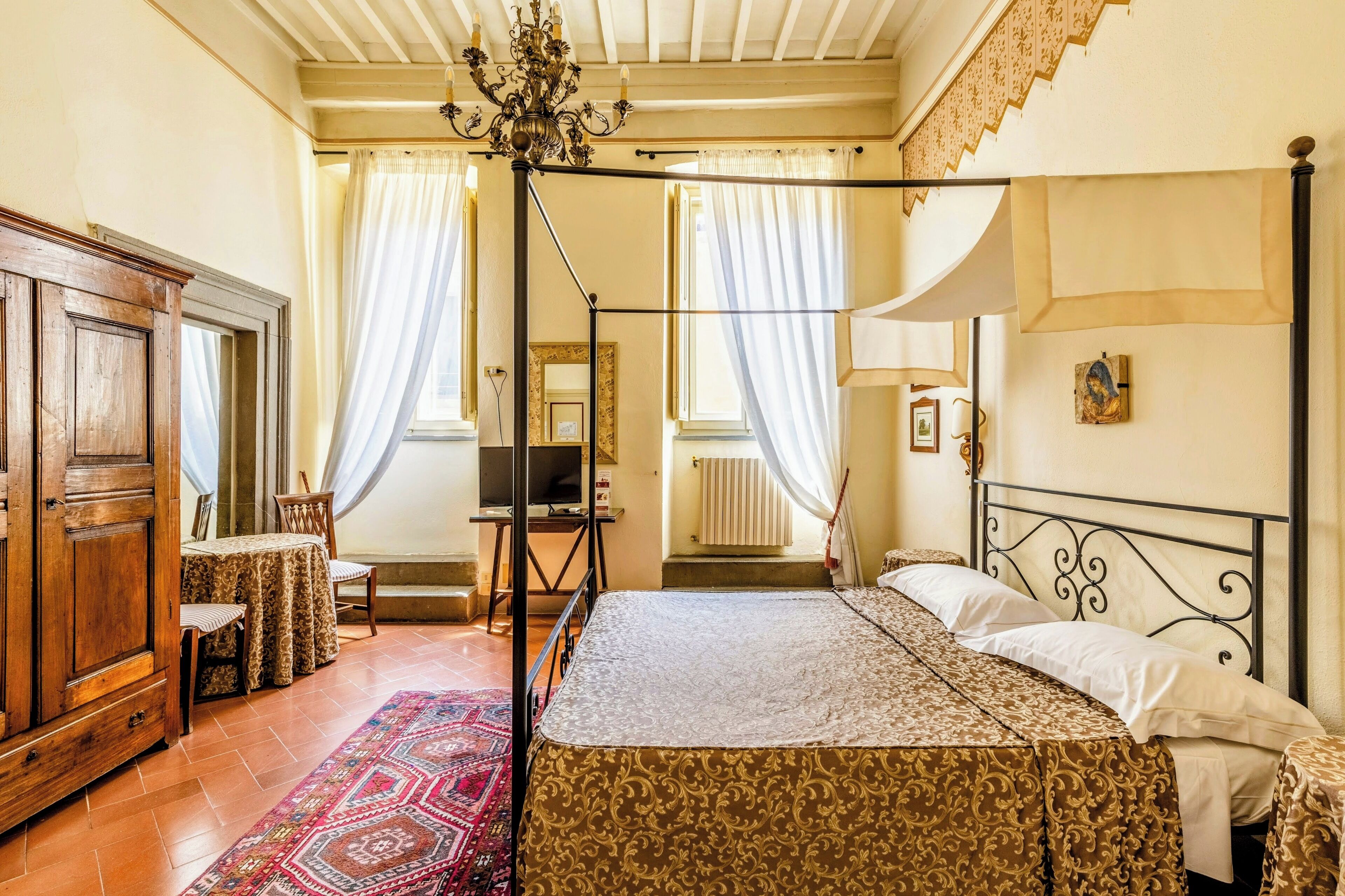 A bedroom with a four-poster bed, a wooden wardrobe, a television, and a small table with chairs.