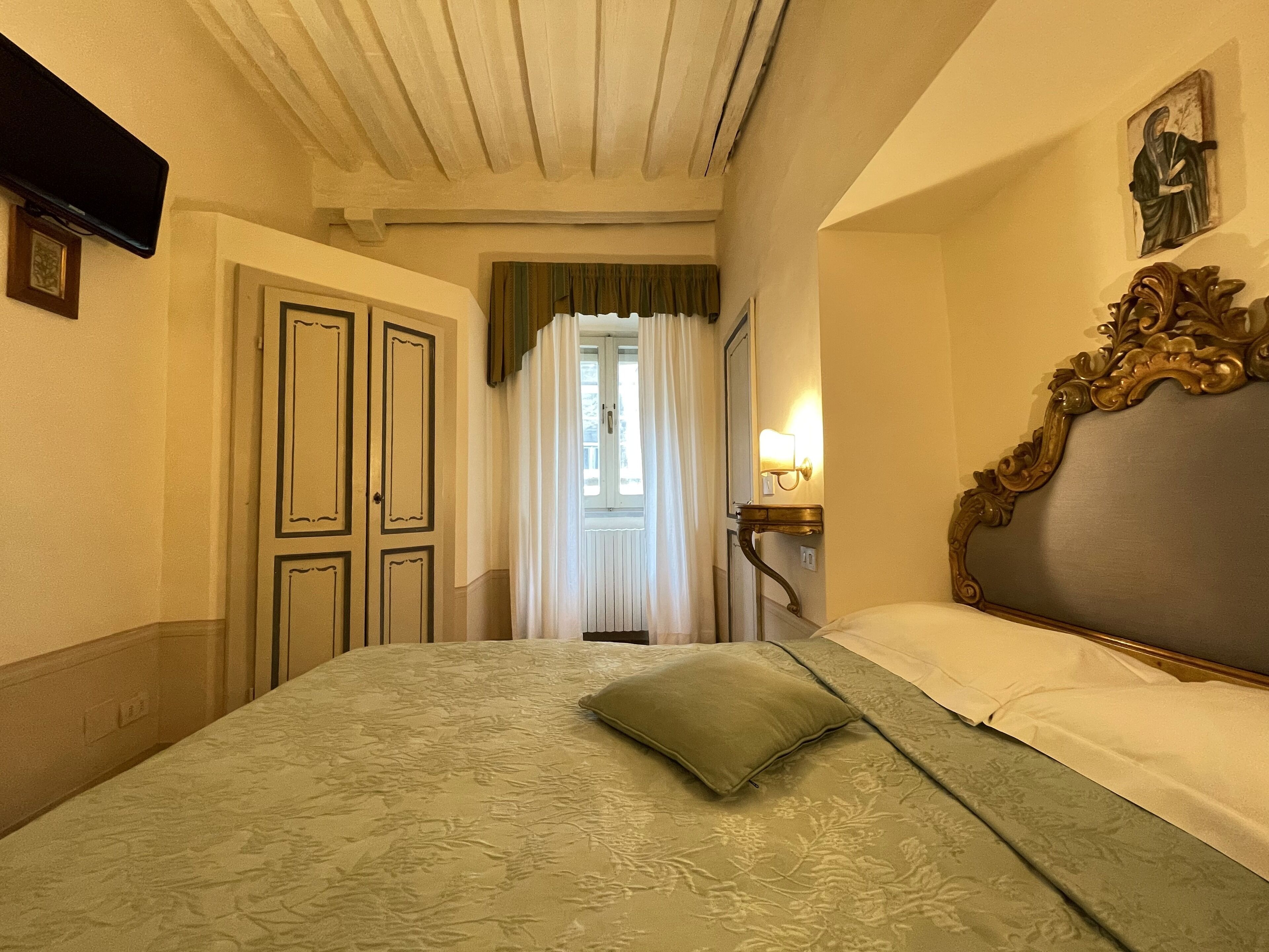Habitación de hotel con cama, mesita de noche, espejo y ventana con cortinas.