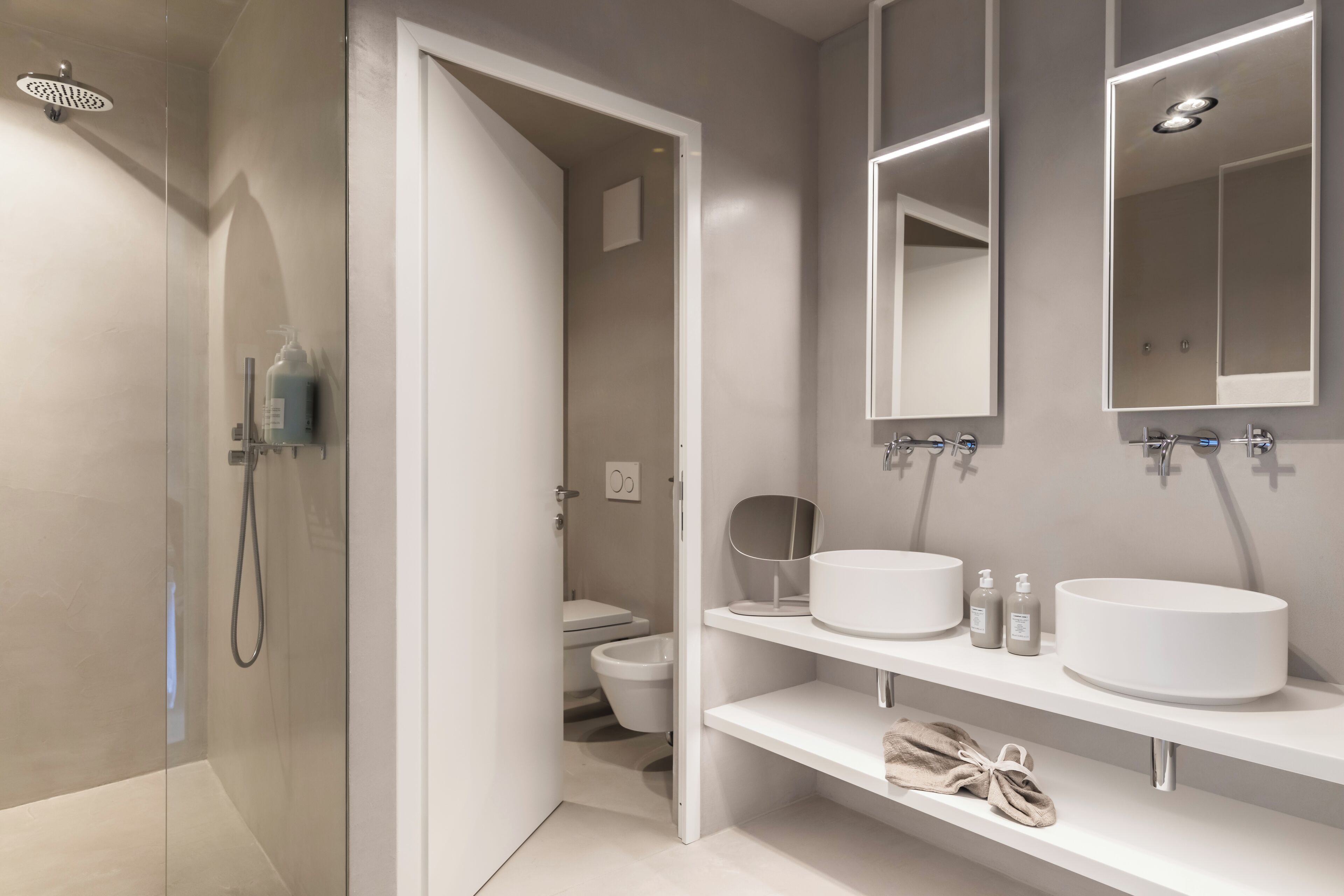 Ein modernes Badezimmer mit einer Duschkabine, einem weißen Waschbecken mit Spiegel darüber und einer Toilette, die durch eine offene Tür sichtbar ist.