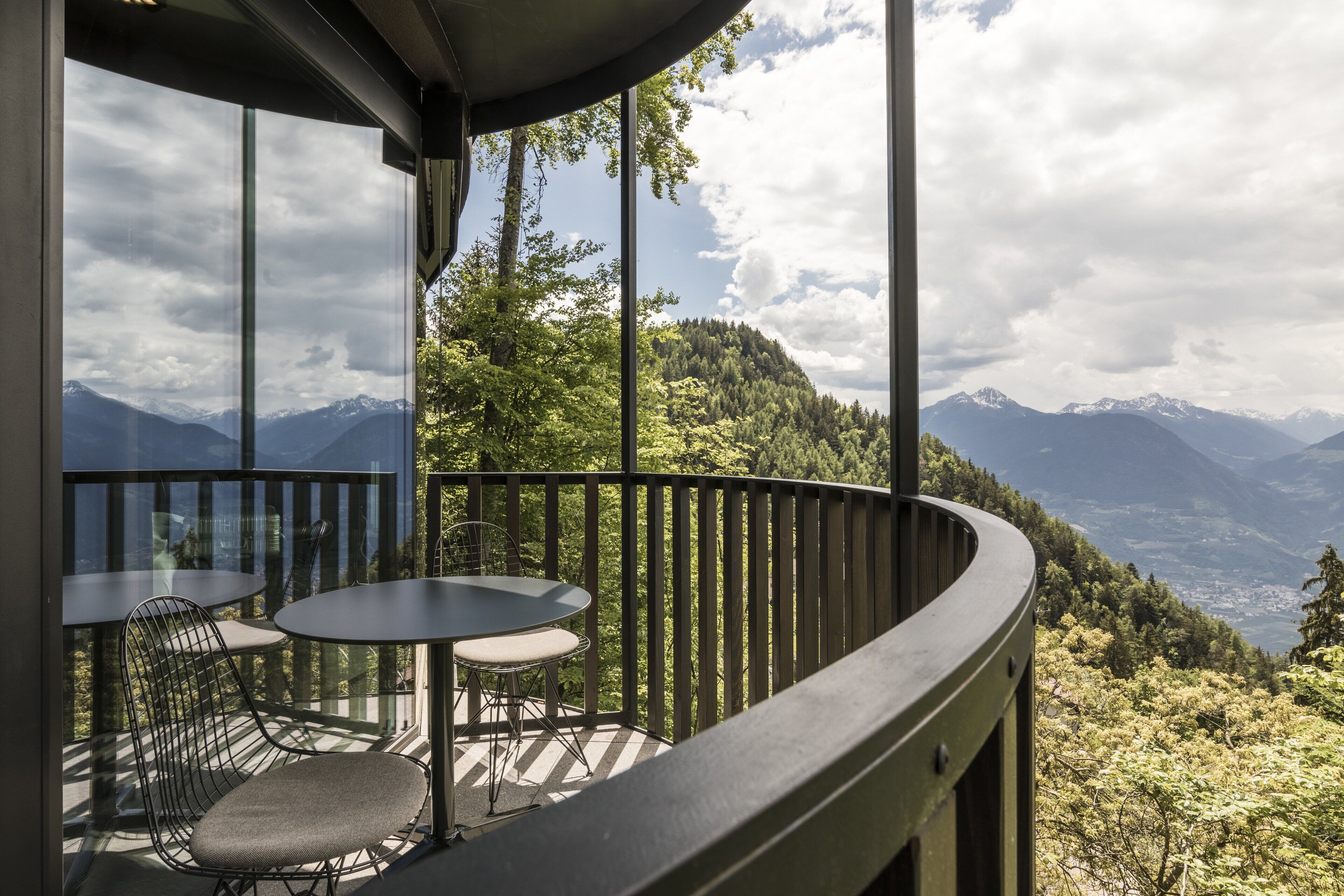 A balcony with a table and chairs, overlooking a mountainous landscape.