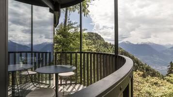 A balcony with a table and chairs, overlooking a mountainous landscape.