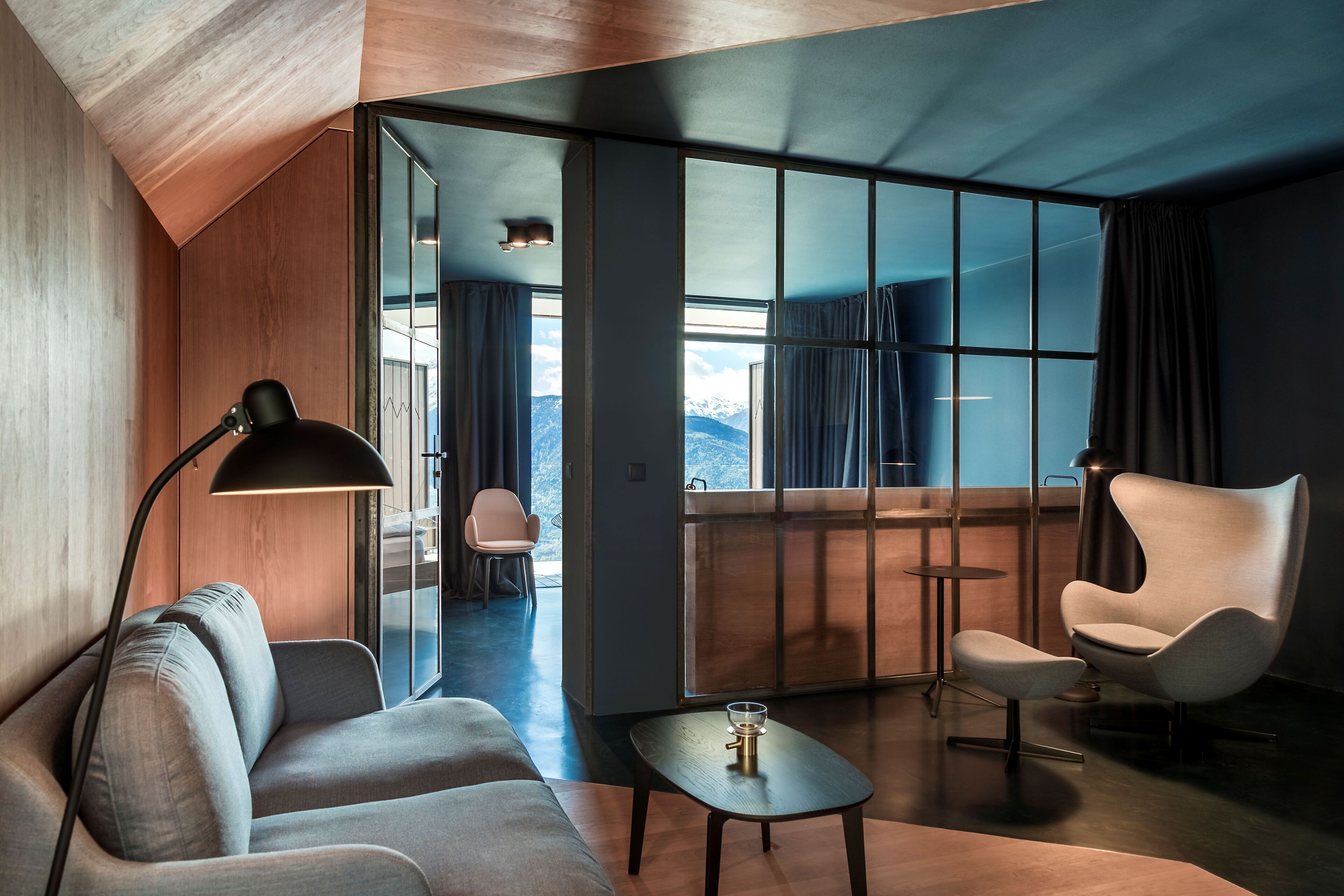 A modern living room with a sofa, armchair, and coffee table, a floor lamp, and a view of a balcony with curtains.
