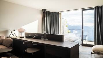 Une chambre d’hôtel moderne équipée d’un bureau, de chaises, d’un lit et d’un balcon offrant une vue sur la montagne.