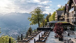 A terrace with sun loungers overlooking a mountainous landscape.