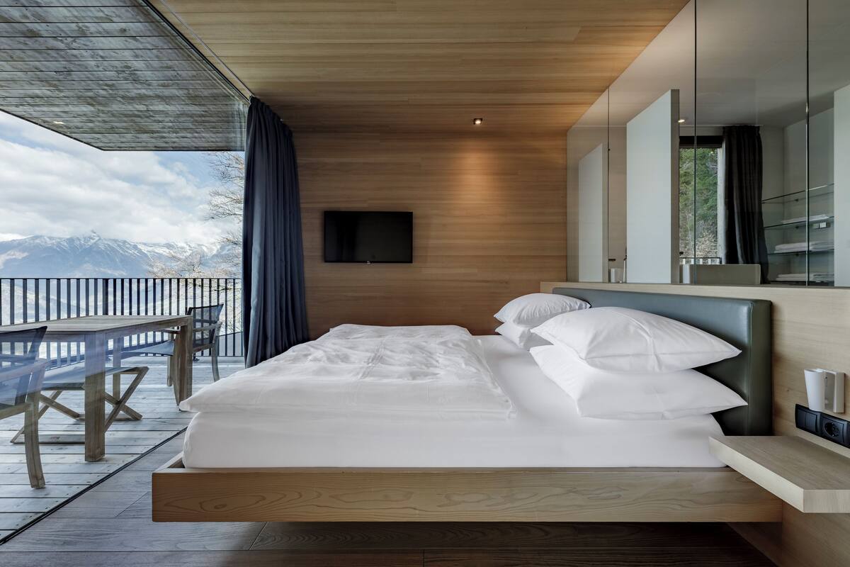 Ein modernes Schlafzimmer mit einem Holzbett, einem Wand-Fernseher und Bergblick.