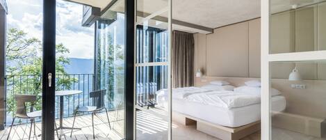 A modern hotel room with a balcony, a bed, and a view of the outdoors.