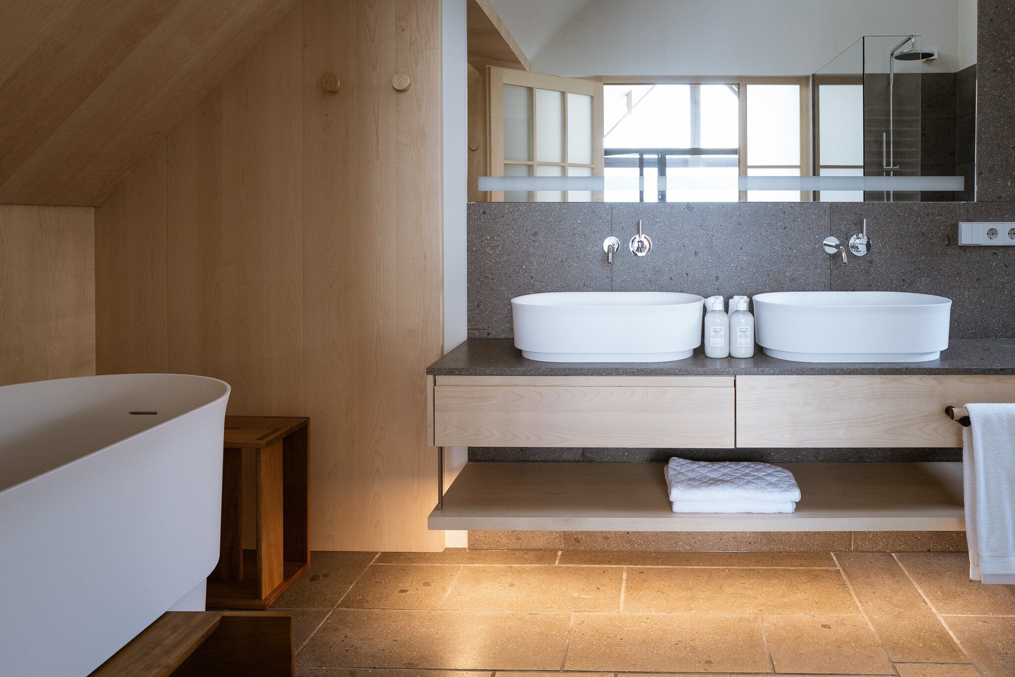 A modern bathroom with a freestanding bathtub, two sinks, a large mirror, and a wooden vanity.