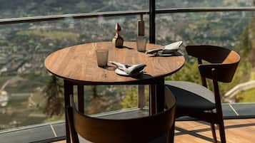 A round wooden table with two chairs, a glass, and a napkin on a balcony with a mountain view.