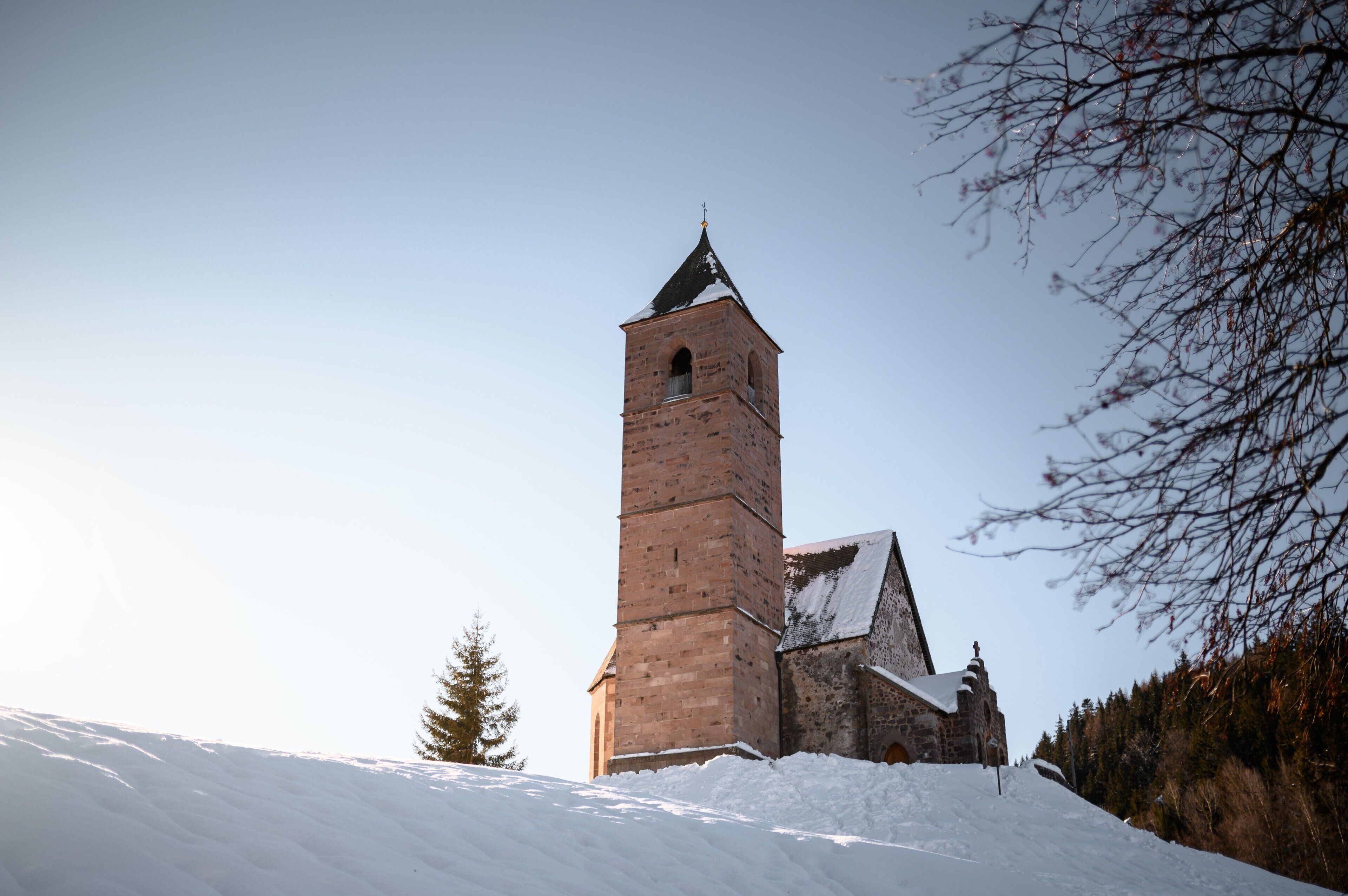 Una chiesa storica con un campanile alto e un edificio in pietra con tetto spiovente.