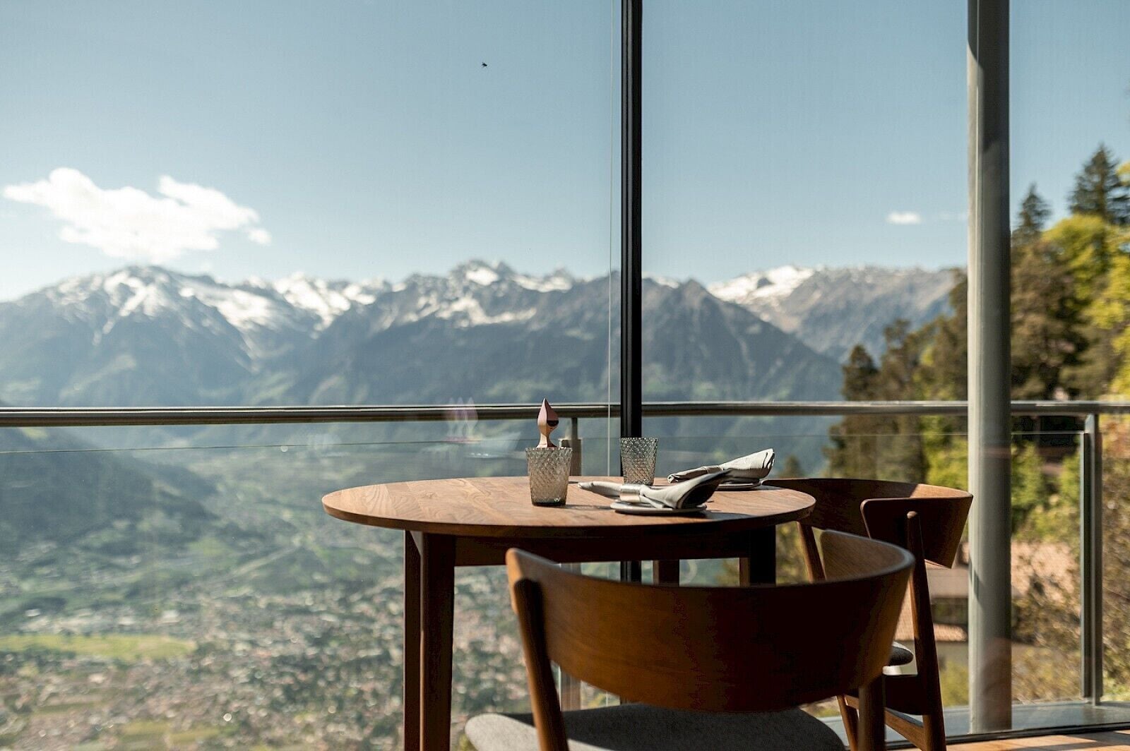 Ein Essbereich mit Tisch und Stühlen, Blick auf verschneite Berge und einer Glasbrüstung.