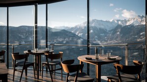 A restaurant with a panoramic mountain view, featuring round tables and chairs.