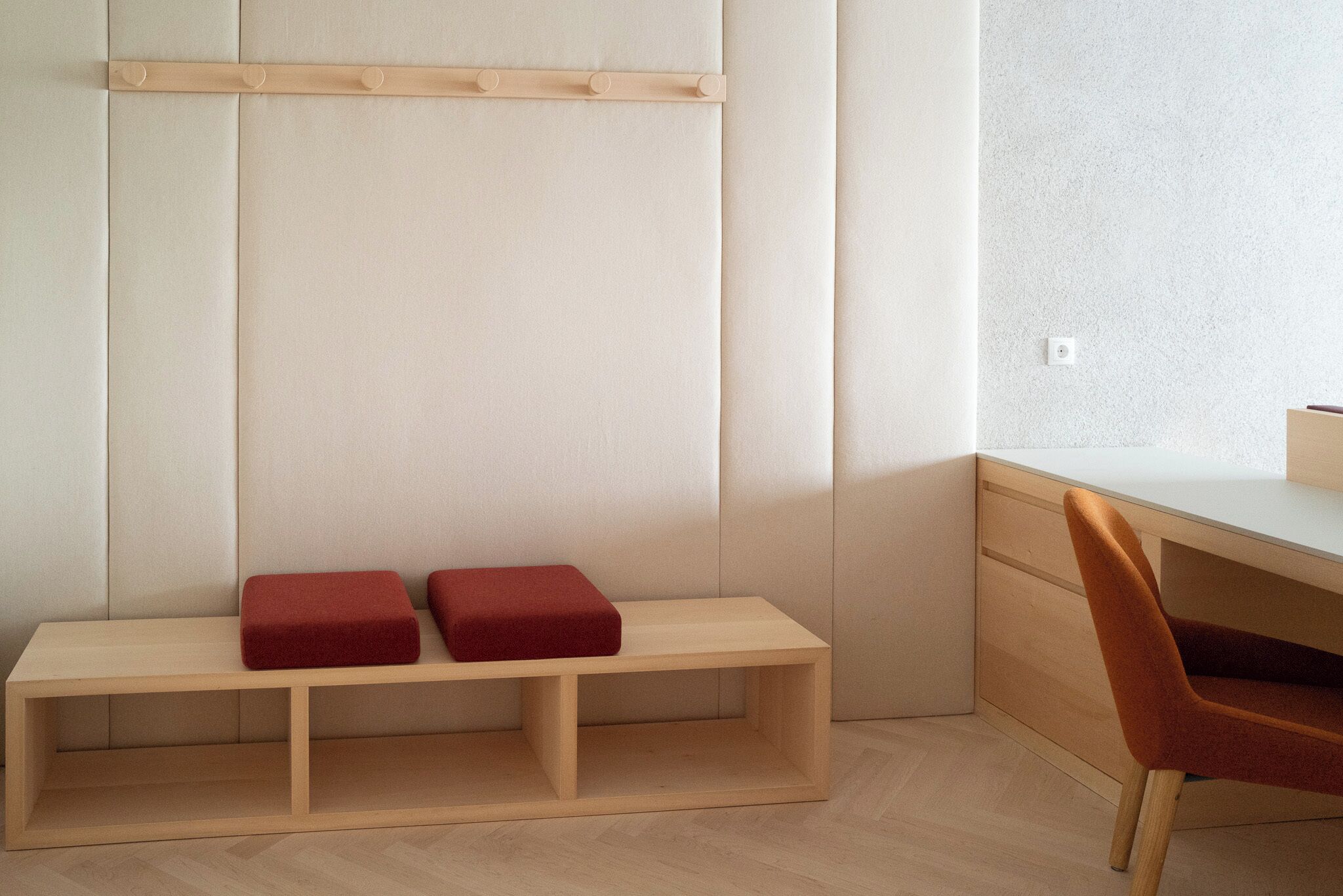 A minimalist room with a wooden bench, a red cushion, and a wooden desk with a chair.