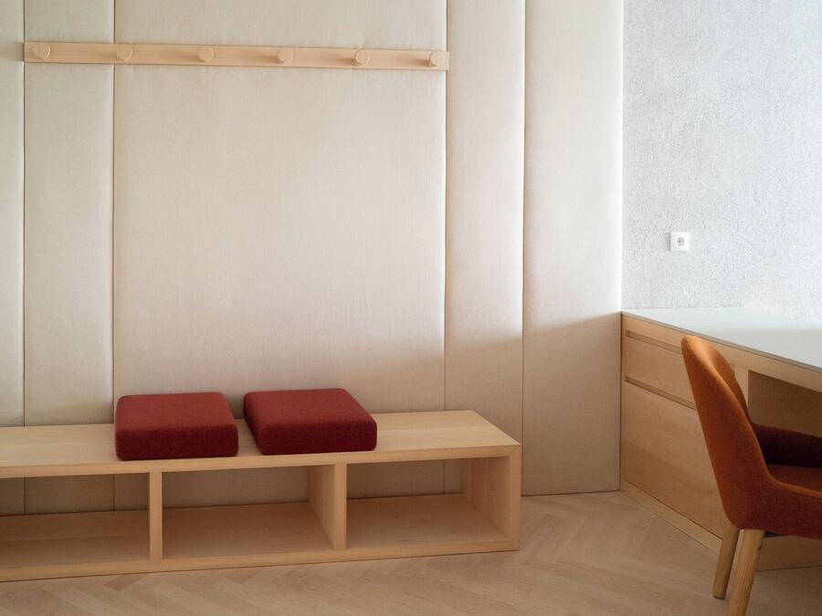 A minimalist room with a wooden bench, a red cushion, and a wooden desk with a chair.