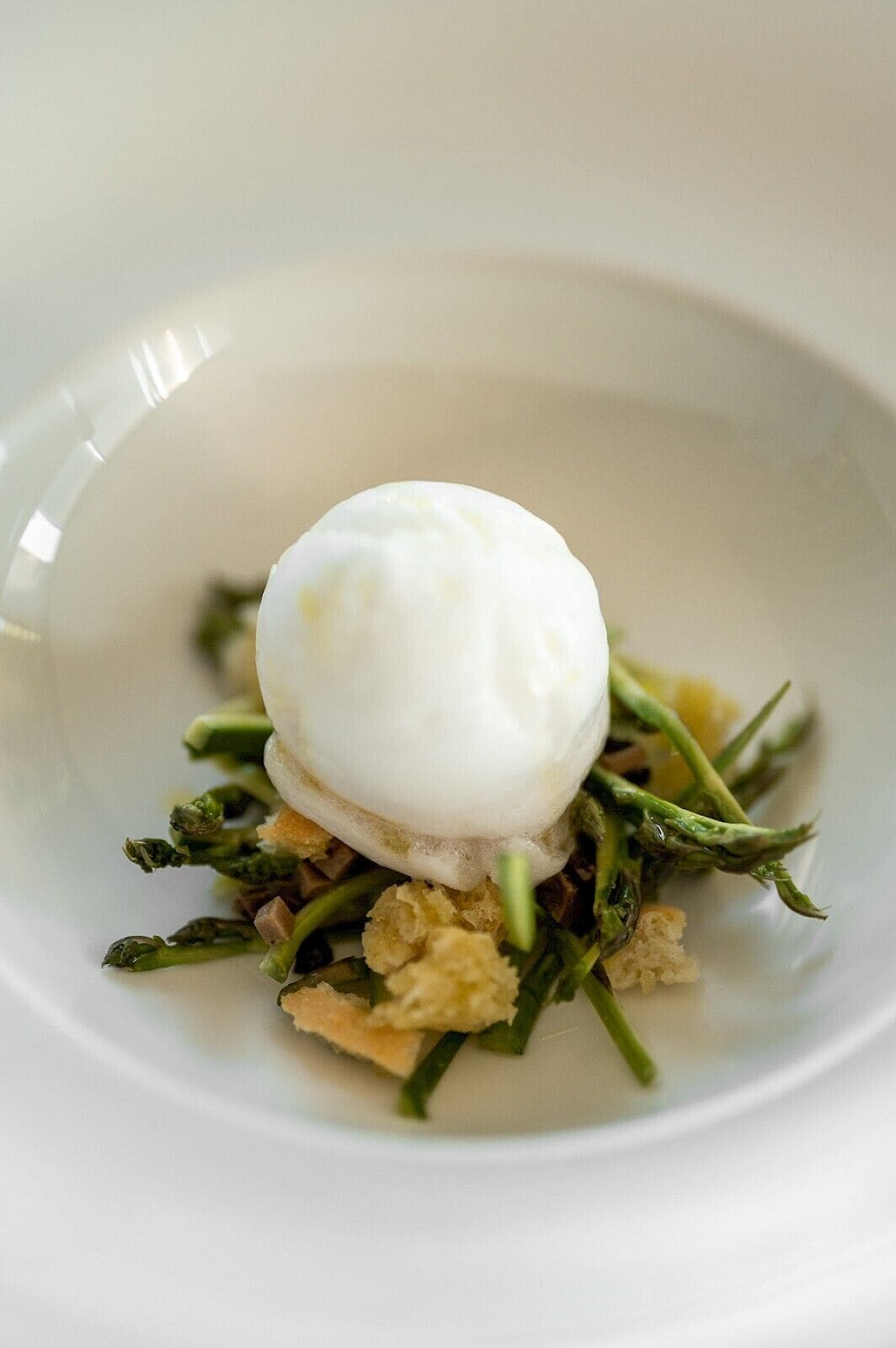 A white plate with a poached egg on top of asparagus and croutons.