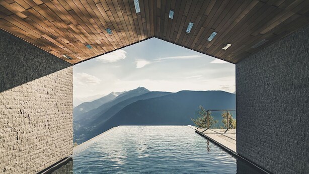A modern infinity pool with a mountain view, wooden ceiling, and stone walls.