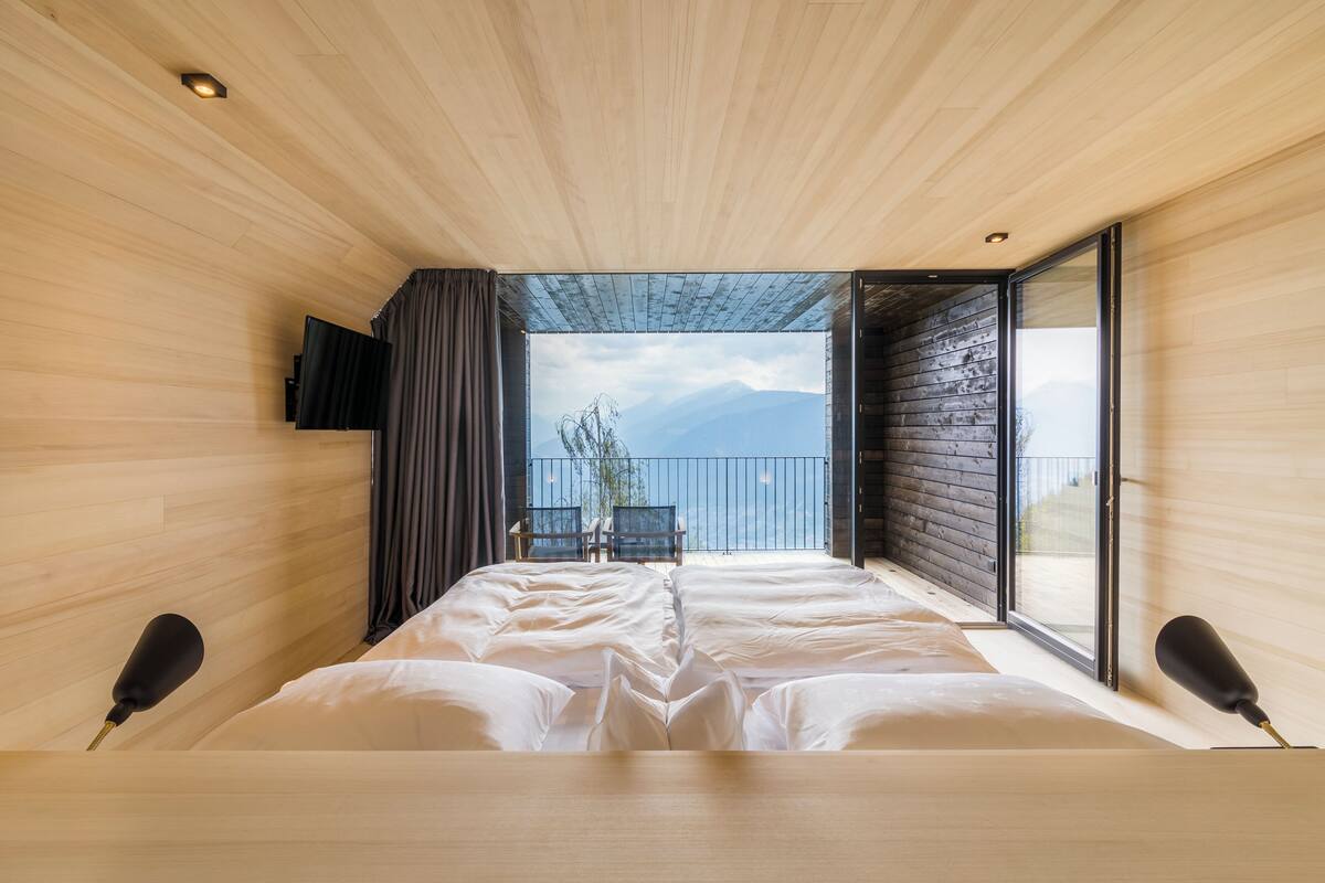 Ein Schlafzimmer mit einem großen Bett, einem an der Wand montierten Fernseher und Blick ins Freie durch eine Schiebetür.
