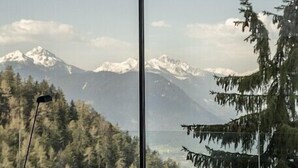 A room with a bed, a small table, and a view of mountains and trees.