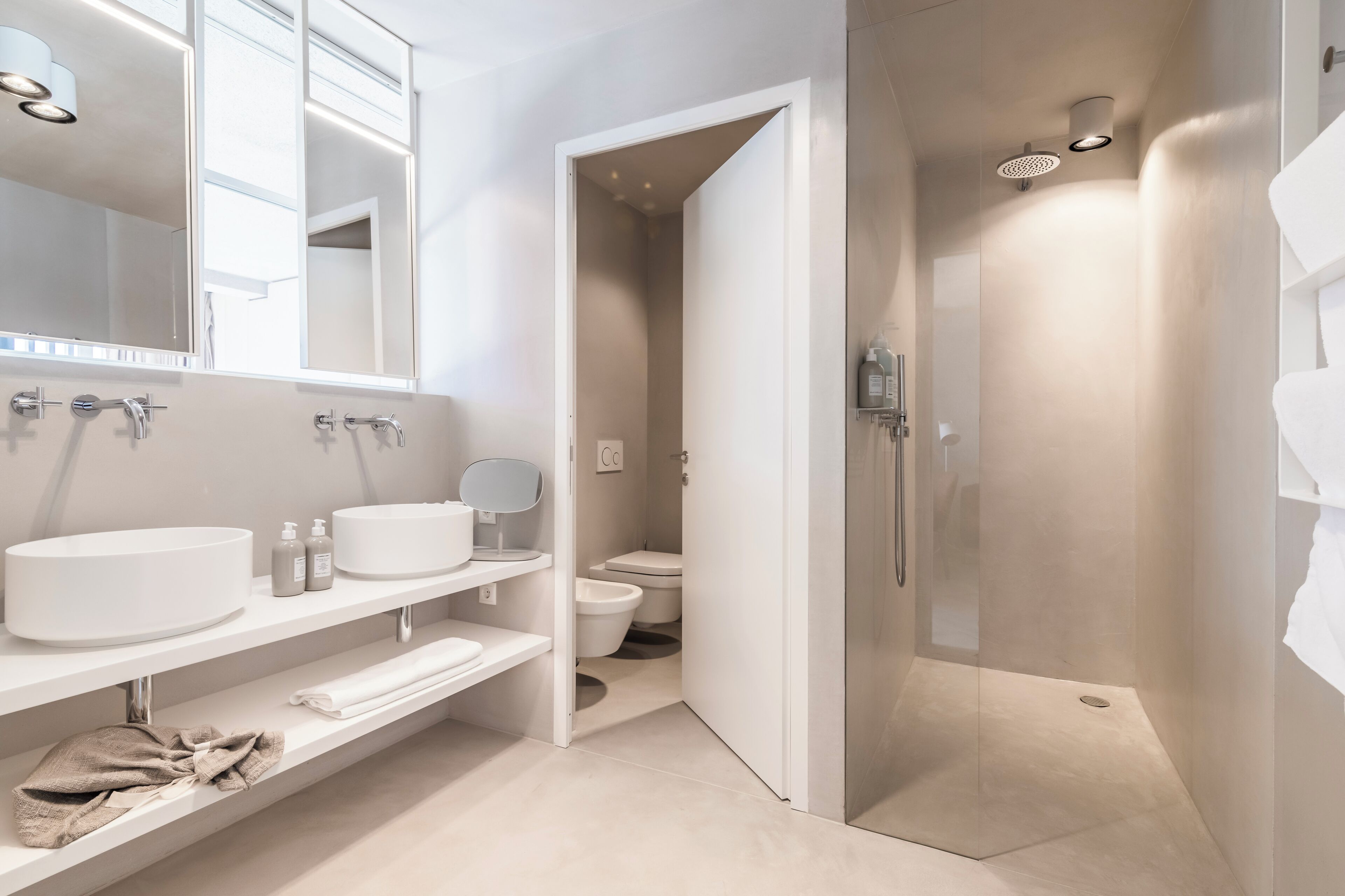 A modern bathroom with a large mirror, two sinks, a shower enclosure, and a toilet.