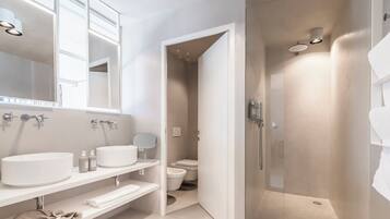 A modern bathroom with a large mirror, two sinks, a shower enclosure, and a toilet.