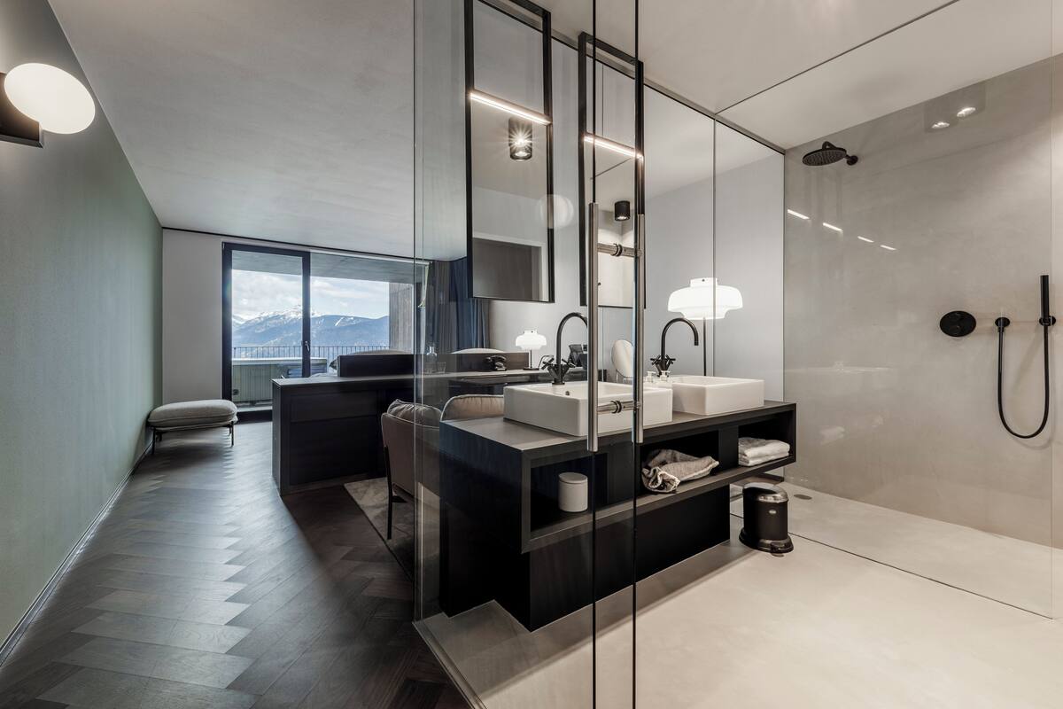 Ein modernes Badezimmer mit großem Spiegel, zwei Waschbecken, einer Dusche und Bergblick durch das Fenster.