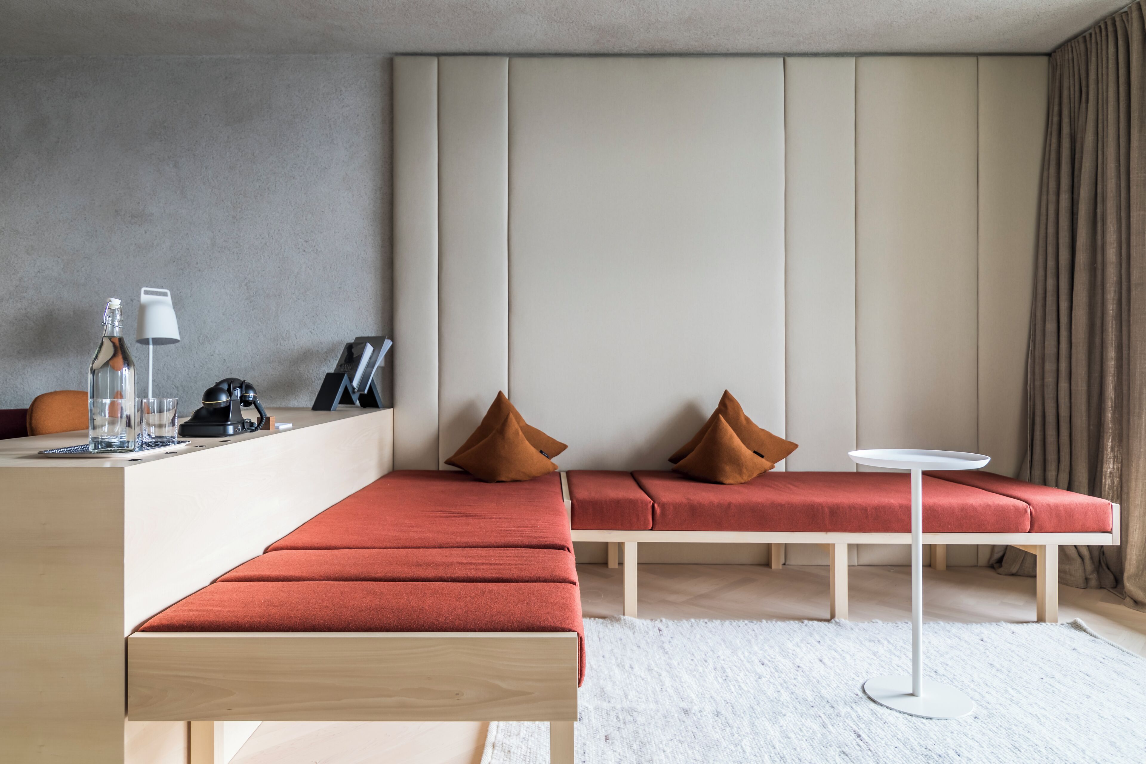 Ein modernes Hotelzimmer mit einem Holztisch, einem kleinen runden Tisch, einer Bank und einem Sofa mit Kissen.