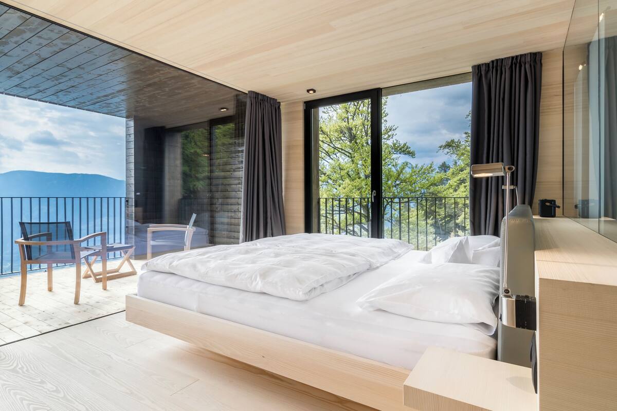 Ein modernes Schlafzimmer mit einem großen Bett, einem Balkon mit Bergblick und einer Sitzecke mit Stühlen.