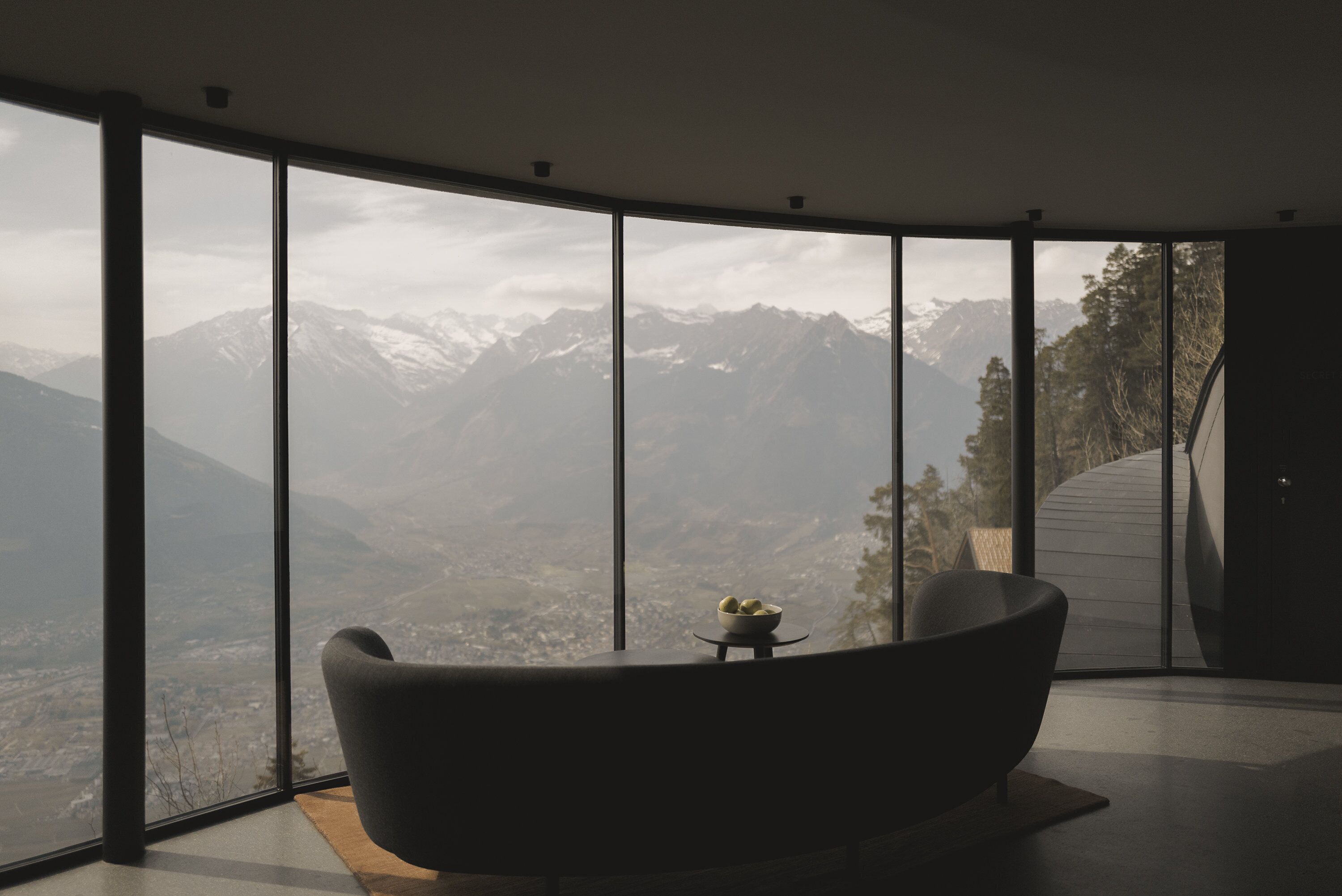 A modern room with a large panoramic window, a black bathtub, and a small table with a bowl of fruit.