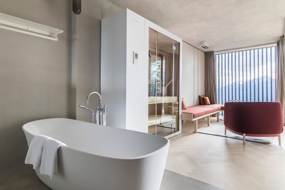 Ein modernes Badezimmer mit einer freistehenden Badewanne, einer gläsernen Duschkabine und Bergblick durch große Fenster.