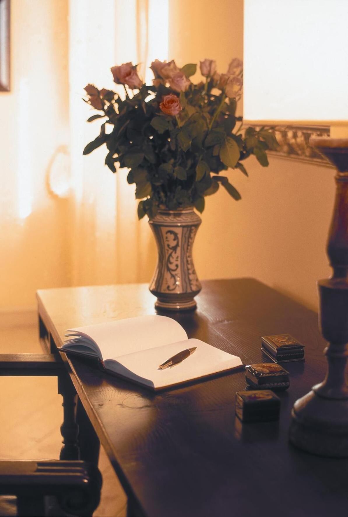 A wooden table with a vase of flowers, a book, and a pen.