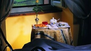 A room with a bed, a small table with a vase of flowers, and a view of a castle through a window. - Palazzo Leti Residenza d'Epoca (Spoleto)