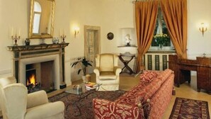 A room with a fireplace, a sofa, a chair, a chandelier, and a window with curtains. - Palazzo Leti Residenza d'Epoca (Spoleto)