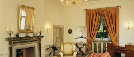 A room with a fireplace, a sofa, a chair, a chandelier, and a window with curtains.