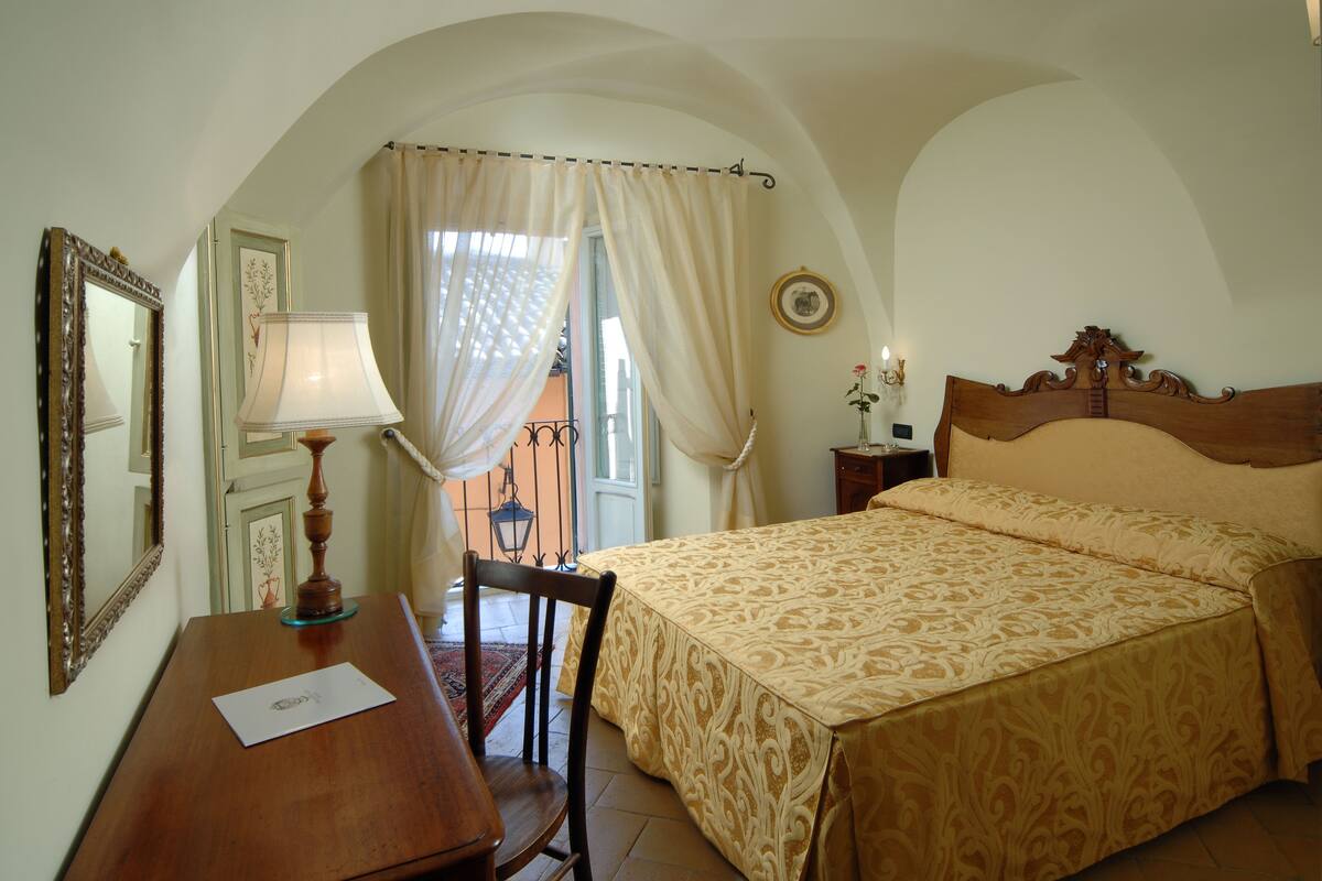 A bedroom with a bed, a desk, a chair, a lamp, and a window with curtains.