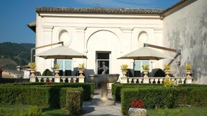 A building with a central entrance, two large umbrellas, and a well-maintained garden with hedges and a pathway leading to the entrance. - Palazzo Leti Residenza d'Epoca (Spoleto)