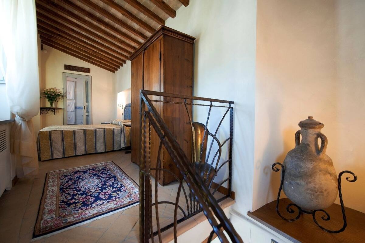A bedroom with a bed, a wooden cabinet, a metal chair, and a decorative vase.