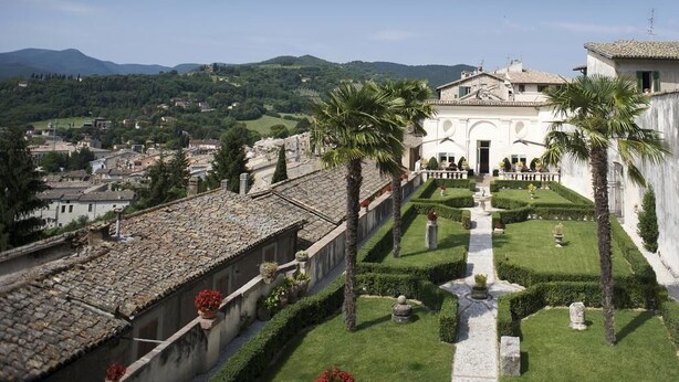 A courtyard with a central pathway, palm trees, and a building with a tiled roof. - Palazzo Leti Residenza d'Epoca (Spoleto)