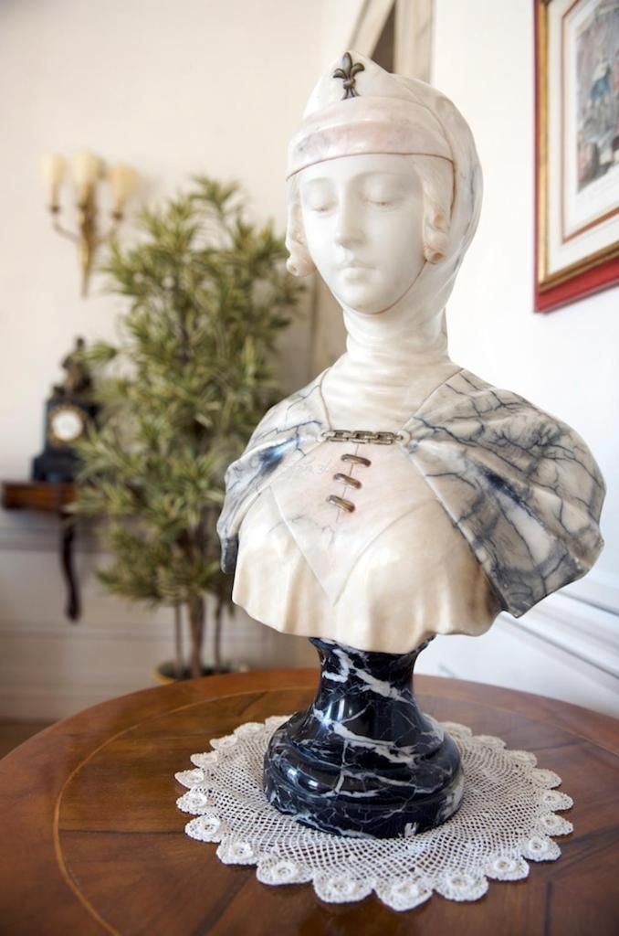 A bust sculpture on a wooden table with a lace doily.